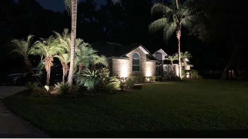 A well-lit home with a manicured lawn and palm trees.
