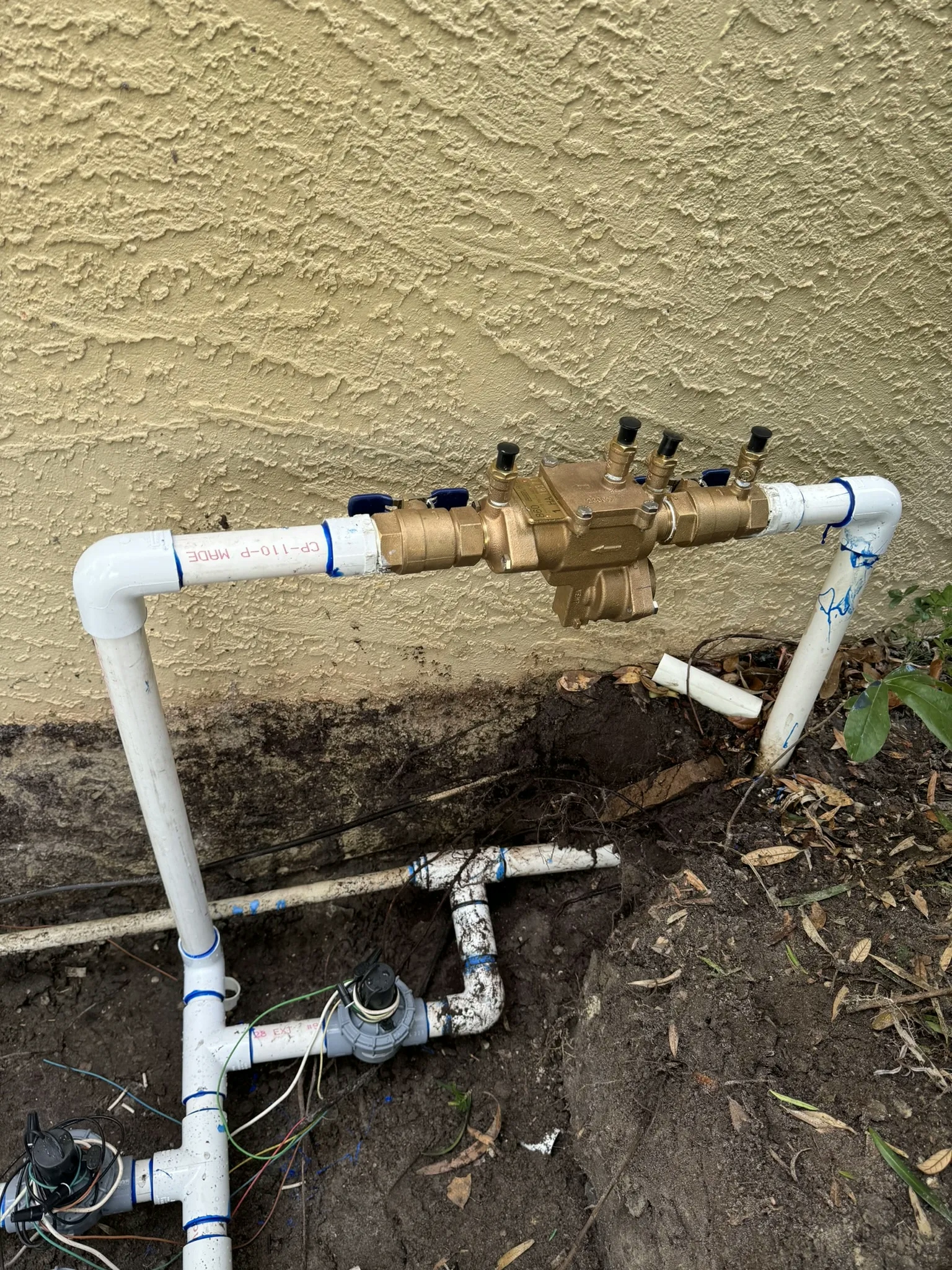 A residential sprinkler system PVC pipes and valves, installed underground near the home's foundation.