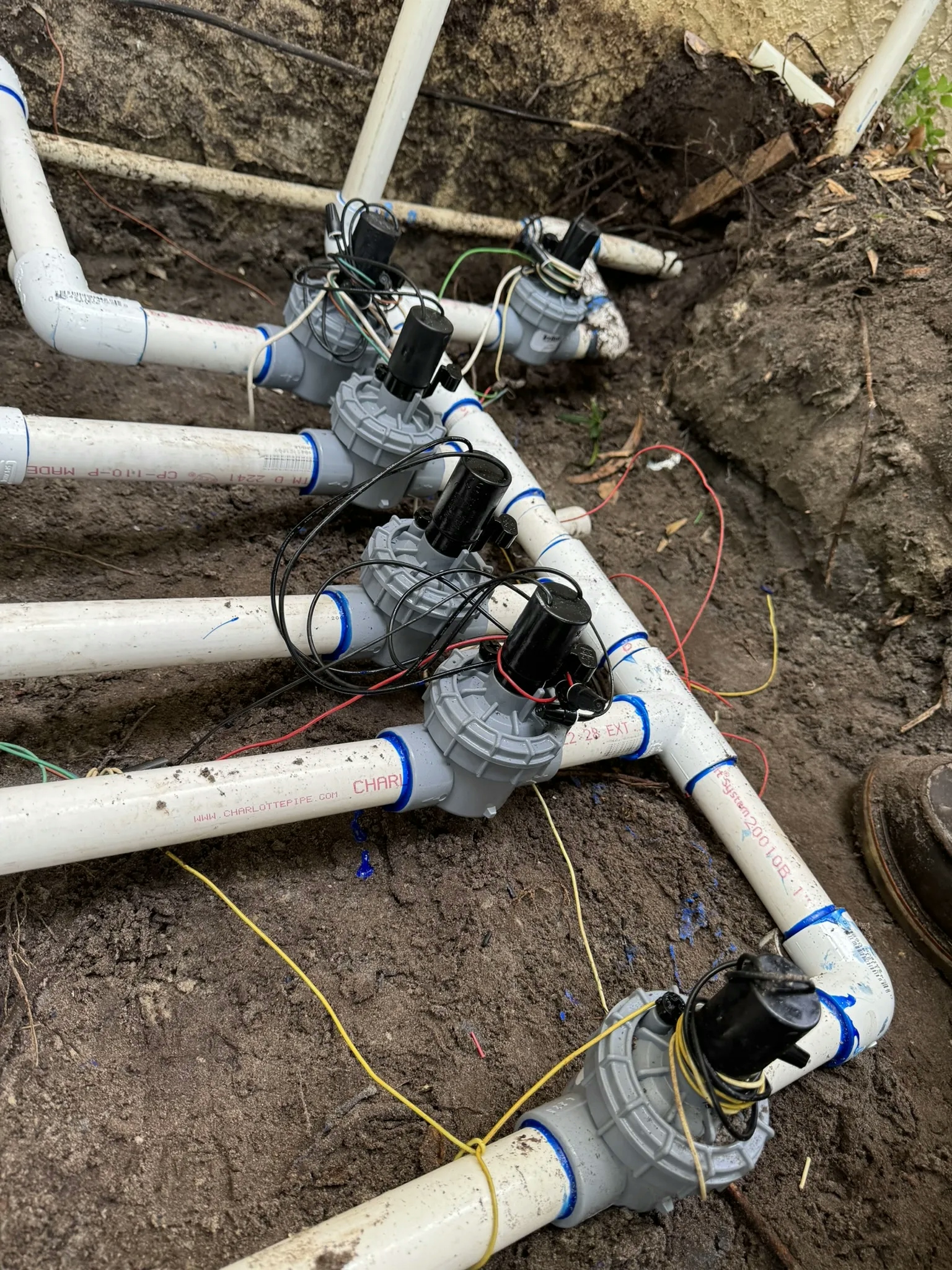 A photo of an irrigation system with white PVC pipes and black electrical wires in a shallow trench in the ground.