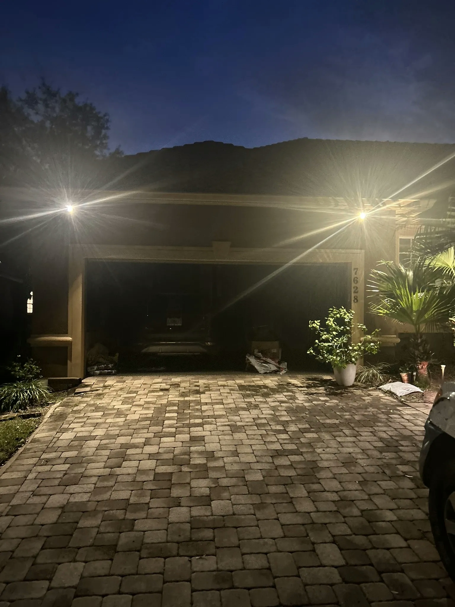 A landscape lighting system illuminates a brick driveway and the exterior of a house at night.